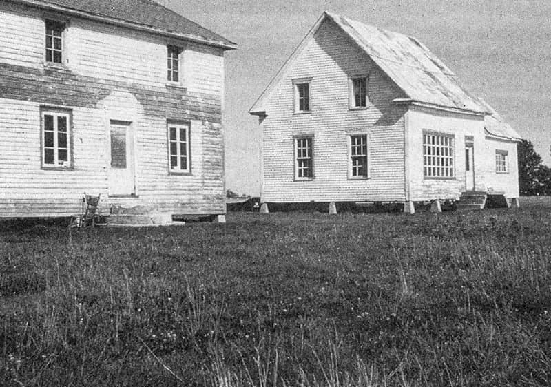 Maisons abandonnées de l’île de Grâce, photo 16 (page 53) dans De Koninck, 1970 : On trouve une dizaine de maisons abandonnées sur l’île de Grâce. Celles que l’on aperçoit sur la photo étaient autrefois situées au centre de l’île. Il y a quelques années, leurs propriétaires, qui quittaient l’île, les transportèrent en chaland, en période de hautes eaux, sur une distance de plus d’un mile, pour les déposer dans la partie la plus élevée de l’île. On remarque les traces laissées par les eaux de débordement.